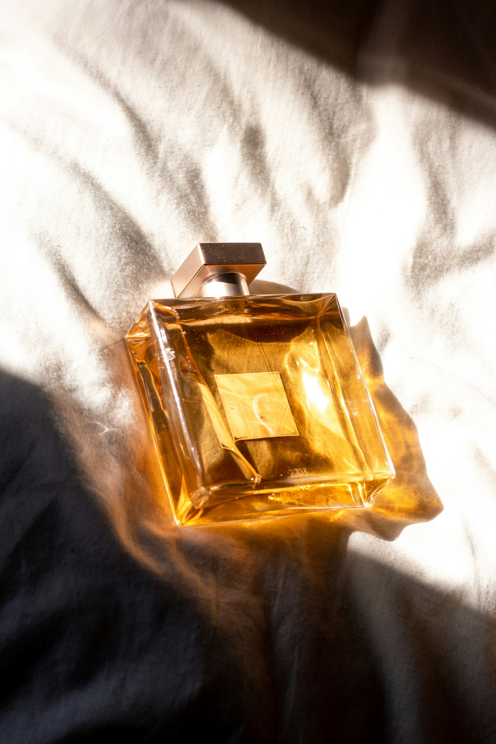 بطری عطر طلایی در دست، روی پارچهٔ کرم