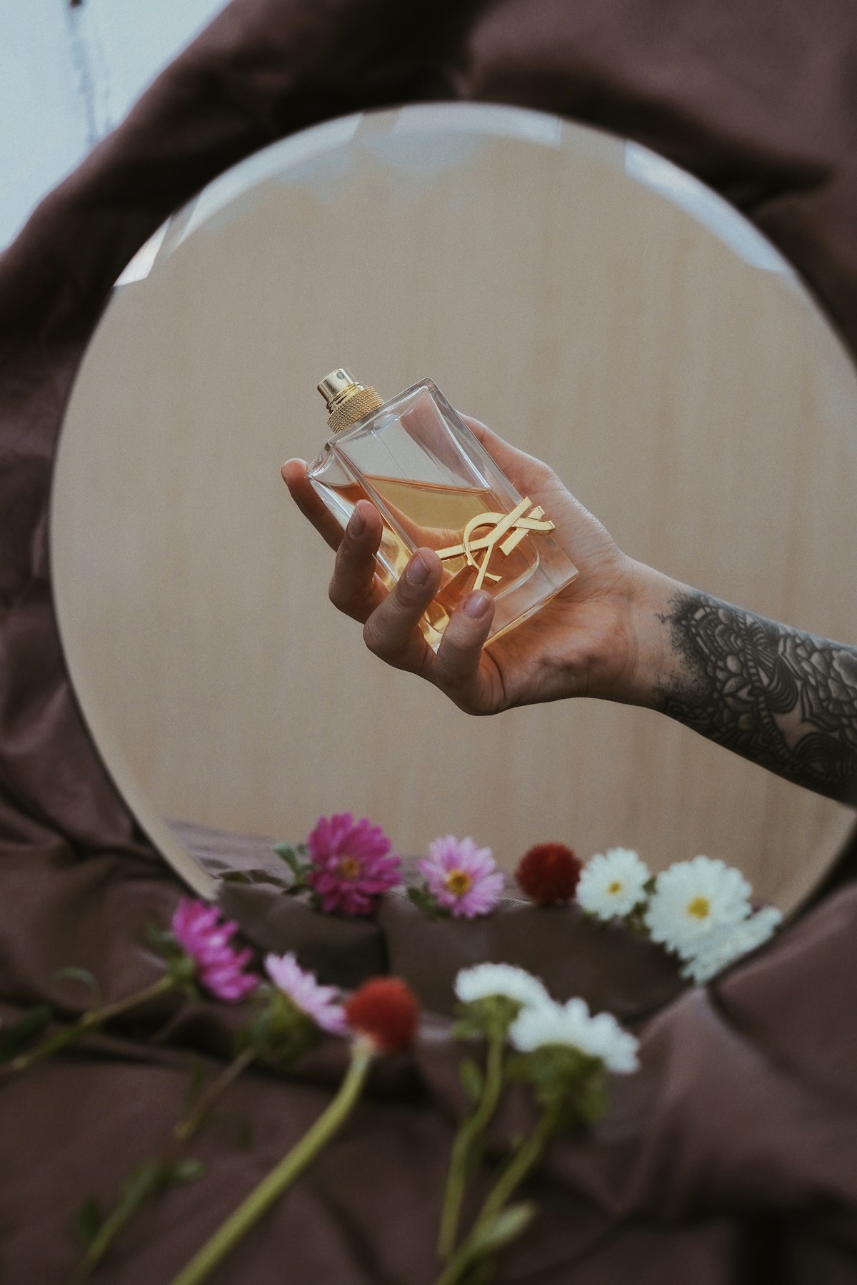 دستی که بطری عطر را کنار گل‌ها نگه داشته